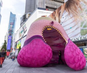A large pink sculpture in Times Square, with buildings and billboards surrounding it.
