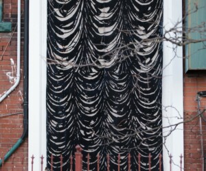 A tall, oversized black and white artwork resembling curtains mounted on the exterior of a brick apartment building