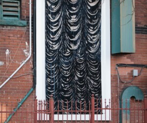 A tall, oversized black and white artwork resembling curtains mounted on the exterior of a brick apartment building