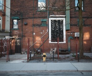 A tall, oversized black and white artwork resembling curtains mounted on the exterior of a brick apartment building