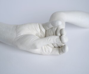 A white ceramic sculpture of an adult hand gently grasping a child's hand against a white background